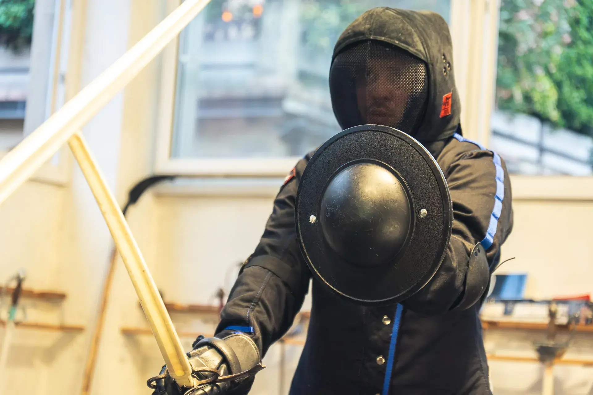 Dettaglio del brocchiero imbracciato da un allievo di Sword Academy, maschera indossata